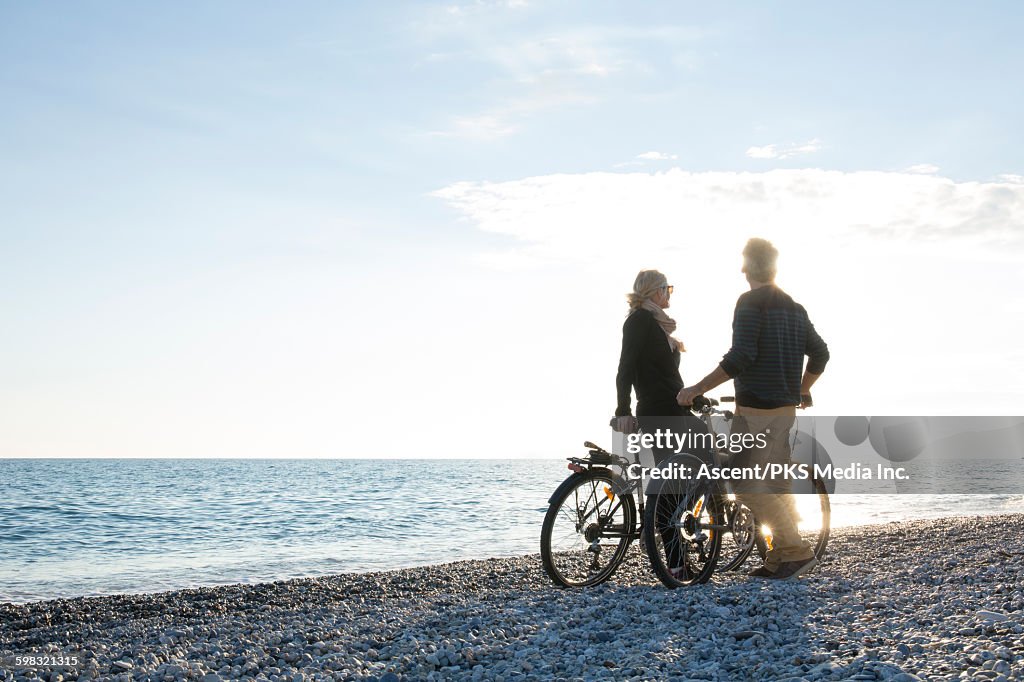 Couple pause with bikes on pebble beach, sunrise