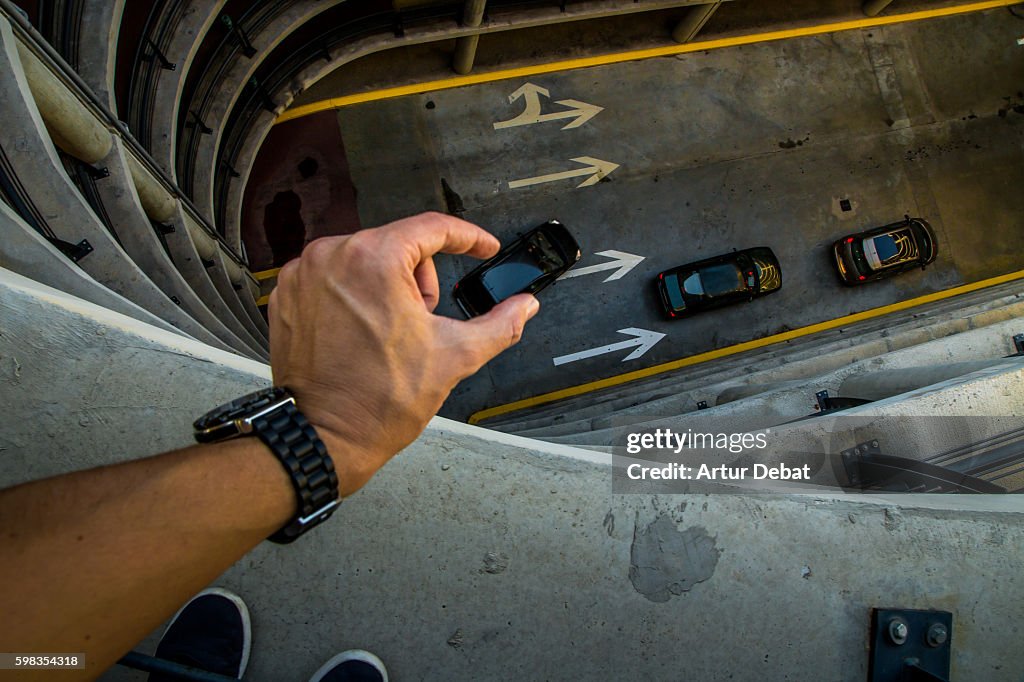 Guy from personal point of view playing with perspective in a nice and creative view in a concrete parking garage holding little cars with his hands like toys.