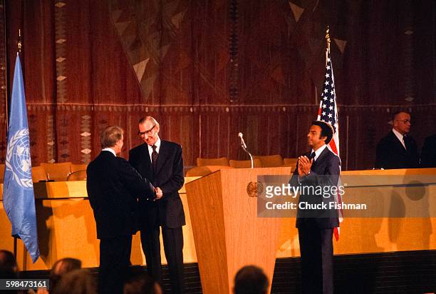 On the floor of the United Nations, American President Jimmy Carter shakes hands UN Secretary General Kurt Waldheim as US Ambassador Andrew Young...