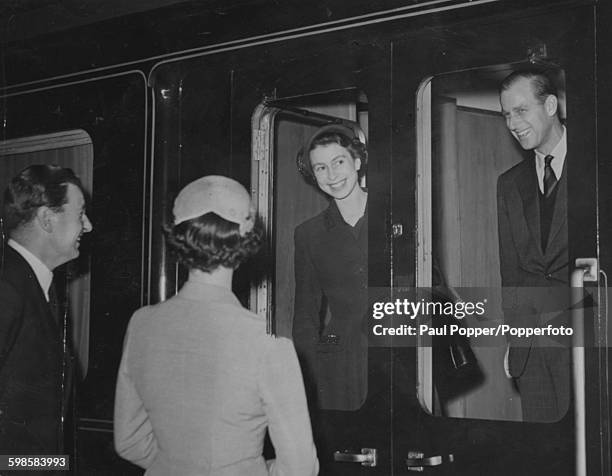 Queen Elizabeth II and Prince Philip, Duke of Edinburgh smiling from the window of their train carriage as they say goodbye to Edward Stanley, 18th...