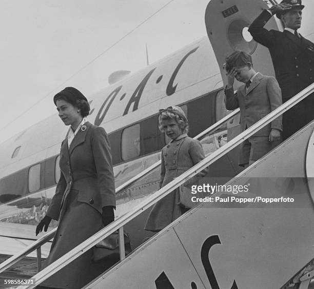 Queen Elizabeth II walks down the steps of a BAOC aircraft with her children, Princess Anne and Prince Charles, after saying goodbye to the Duke of...