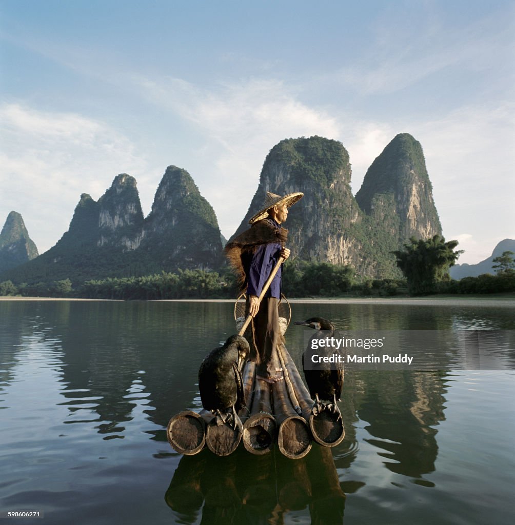 Comorant fisherman standing on bamboo raft