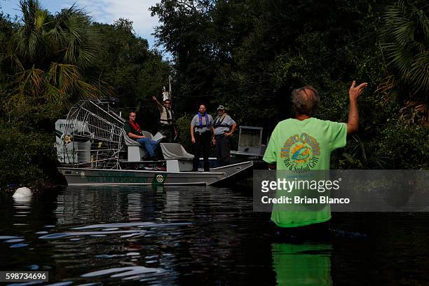 Resident points back to his home as he speaks with law enforcement officers using an airboat to survey damage around homes from high winds and storm...
