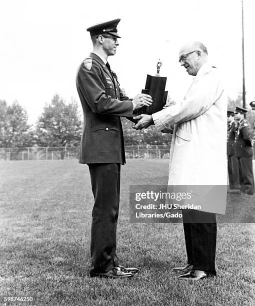 On the grassy Homewood Field at Johns Hopkins University, President Milton Stover Eisenhower wears a trench coat and glasses while presenting the...