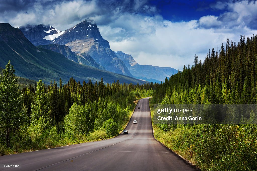 Two-lane famous Icefields Parkway between Lake Louise and Jasper, Alberta, with snowcapped mountains looming above in summer
