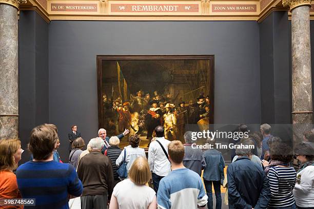 Visitors in a tour group view famous painting by Rembrandt 'The Night Watch' at Rijksmuseum in Amsterdam, Holland.