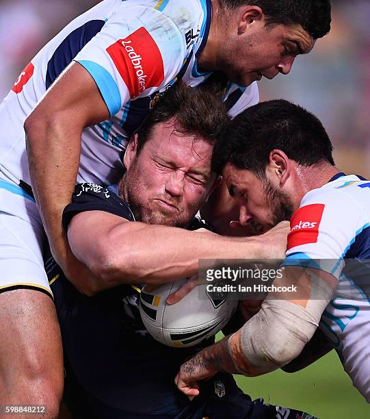 Gavin Cooper of the Cowboys is tackled by Nathan Peats and Ashley Taylor of the Titans during the round 26 NRL match between the North Queensland...