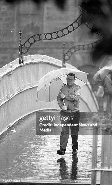 Dubliners cross the Ha' Penny Bridge soaked by the rains from Hurricane Charley, circa August 1986 .