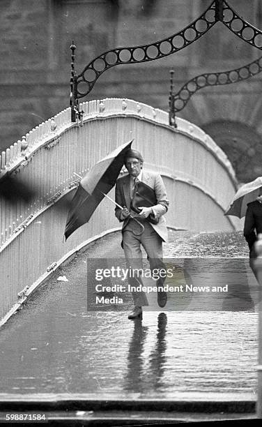 Dubliners cross the Ha' Penny Bridge soaked by the rains from Hurricane Charley, circa August 1986 .