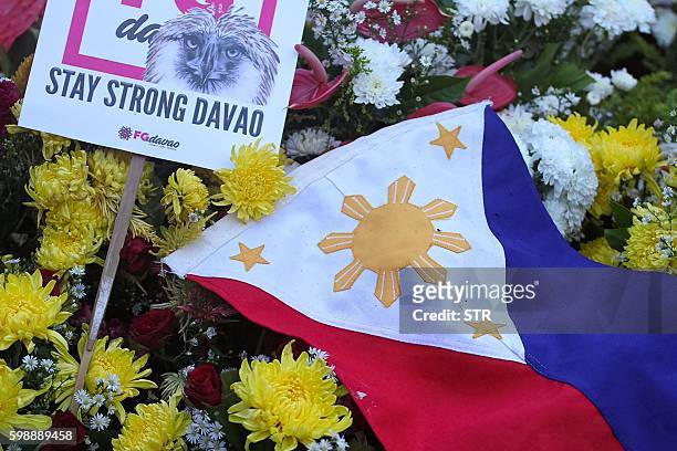 National flag is placed among flowers as residents offer prayers for bomb blast victims at a night market, during a memorial at the site in Davao...