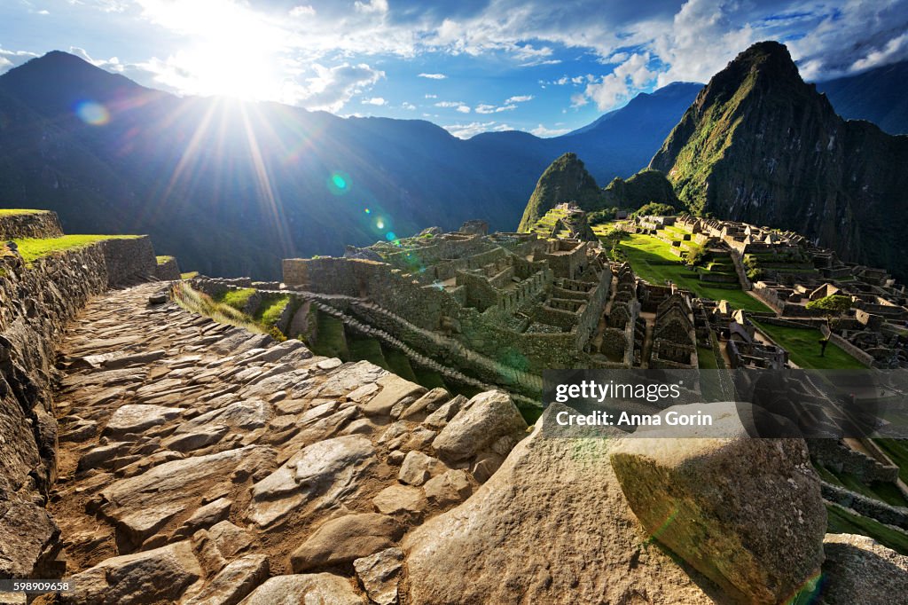 Evening sunburst over deserted paved pathway overlooking Machu Picchu ruins, Peru