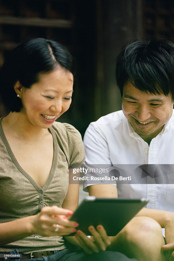 Portrait of a cheerful Japanese couple using tablet outdoors