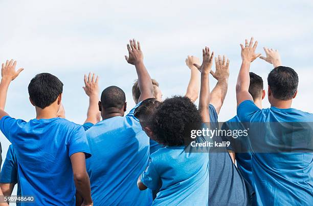 vista posterior multiétnico grupo de voluntarios de plantear las manos - blue shirt fotografías e imágenes de stock
