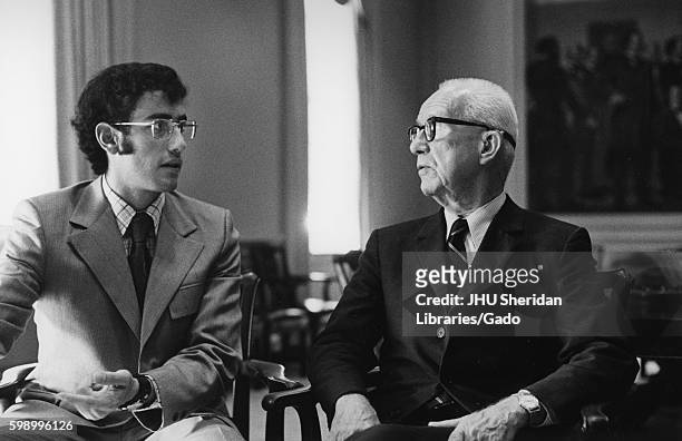 Half-length portrait of architect Buckminster Fuller speaking with another man, Fuller wearing a dark suit with a white shirt and a striped tie,...
