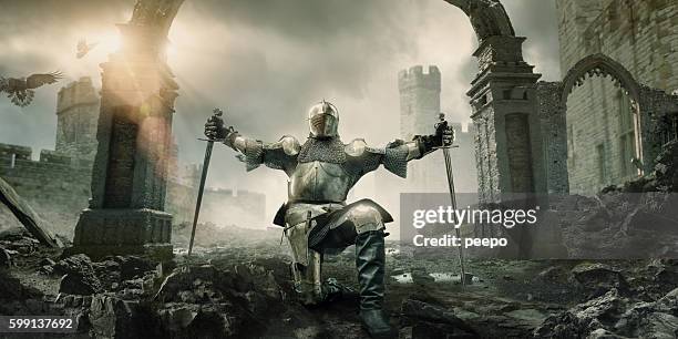 medieval knight kneeling with sword in front of building ruin - harnas stockfoto's en -beelden