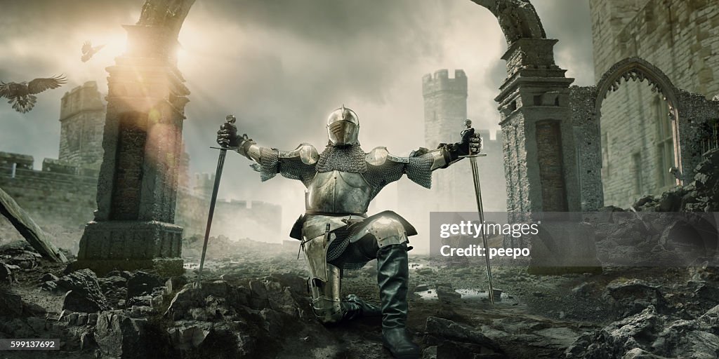 Medieval Knight Kneeling With Sword In Front of Building Ruin