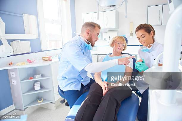 dentist showing senior patient model of dentures - dentures stock pictures, royalty-free photos & images