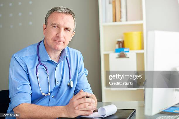 smiling gp sitting at desk - family doctor stockfoto's en -beelden