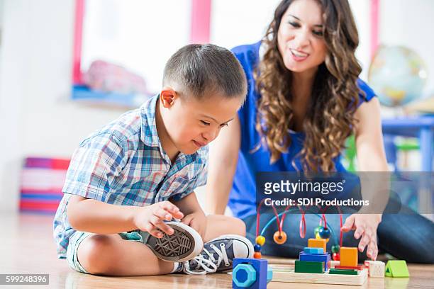 hispanic down syndrome boy reaching for toys at daycare center - special needs children stock pictures, royalty-free photos & images