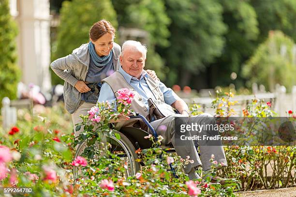 fürsorgliche und senior mann auf einem rollstuhl zu fuß im freien - care stock-fotos und bilder