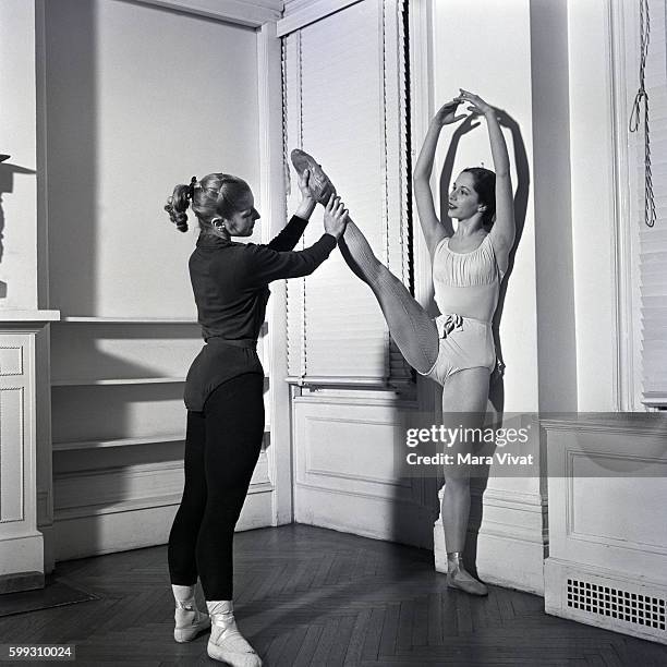 New York City Ballet dancer stretches her legs with assistance from a fellow dancer at a barre in the rehearsal studio. New York City, New York, USA.