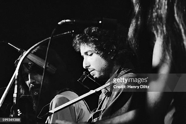 Bob Dylan plays his guitar on stage during the 1971 Concert for Bangladesh. George Harrison is in the background.
