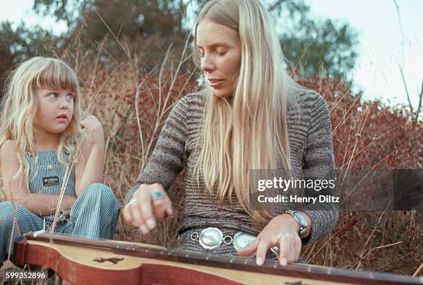 Singer-songwriter Joni Mitchell plays a mountain dulcimer for a little girl outside.