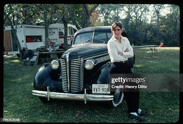 On a motion picture set, Matt Dillon leans against a vintage black car. Published in Bravo Magazine.