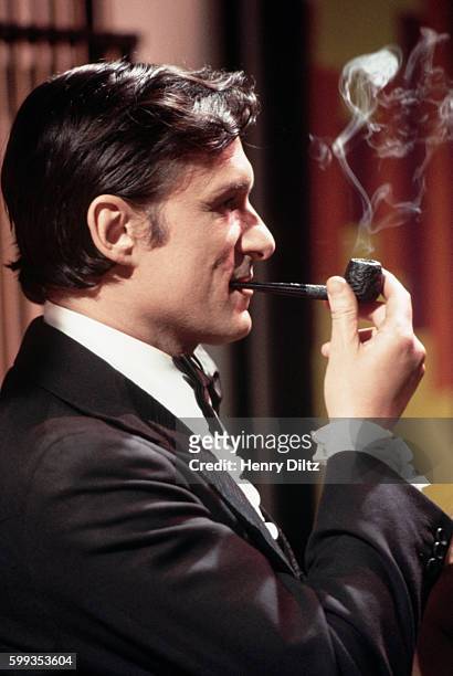Publisher Hugh Hefner smokes his pipe on the sound stage during the filming of his television show Keyhole. Hefner played the role of playboy and...