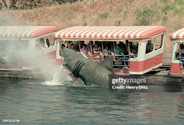 An artificial shark used in the movie, Jaws, jumps from a pond as tourists pass by in a tram on a tour of Universal Studios.
