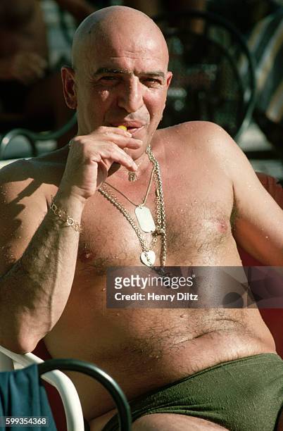 Actor Telly Savalas lounges by a pool.