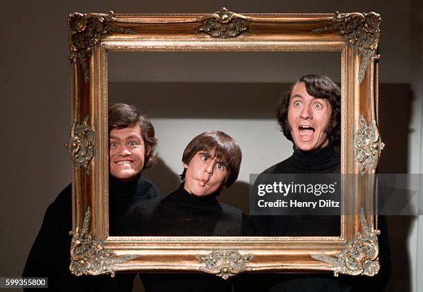 Three of The Monkees make faces behind an empty picture frame.
