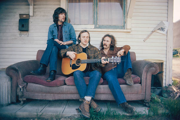 Graham Nash, Stephen Stills, and David Crosby relax outside on an old couch.