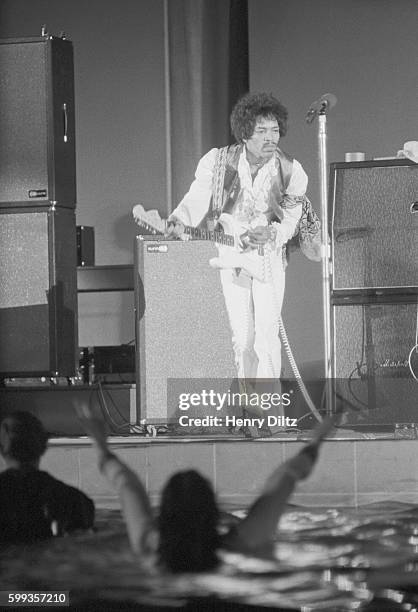 Guitarist Jimi Hendrix playing at Hollywood bowl in 1968. Some fans have jumped into the pond and are waving their arms.