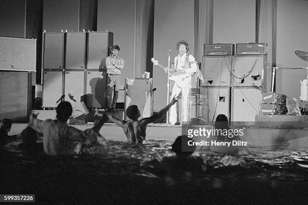 Legendary guitarist Jimi Hendrix playing at Hollywood bowl in 1968. Some fans have jumped into the pond and are waving their arms.