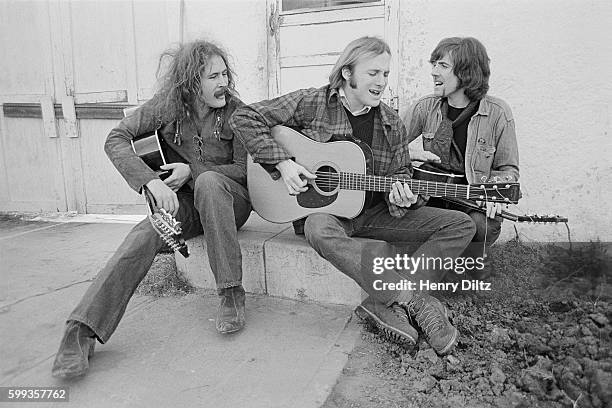 Musicians David Crosby , Stephen Stills , and Graham Nash sing and play their guitars on the porch.