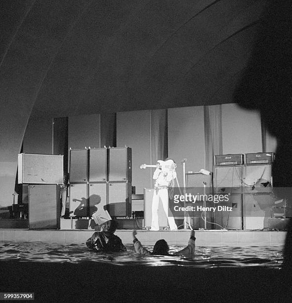 Guitarist Jimi Hendrix playing at Hollywood bowl in 1968. Some fans have jumped into the pond and are waving their arms.