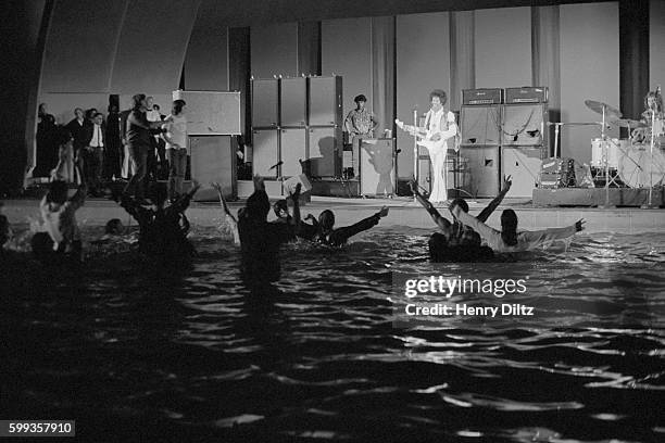 Guitarist Jimi Hendrix playing at Hollywood bowl in 1968. Some fans have jumped into the pond and are waving their arms.