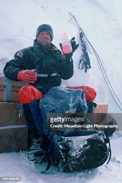 Climber holds up a beverage while sitting in camp on Mount Everest.