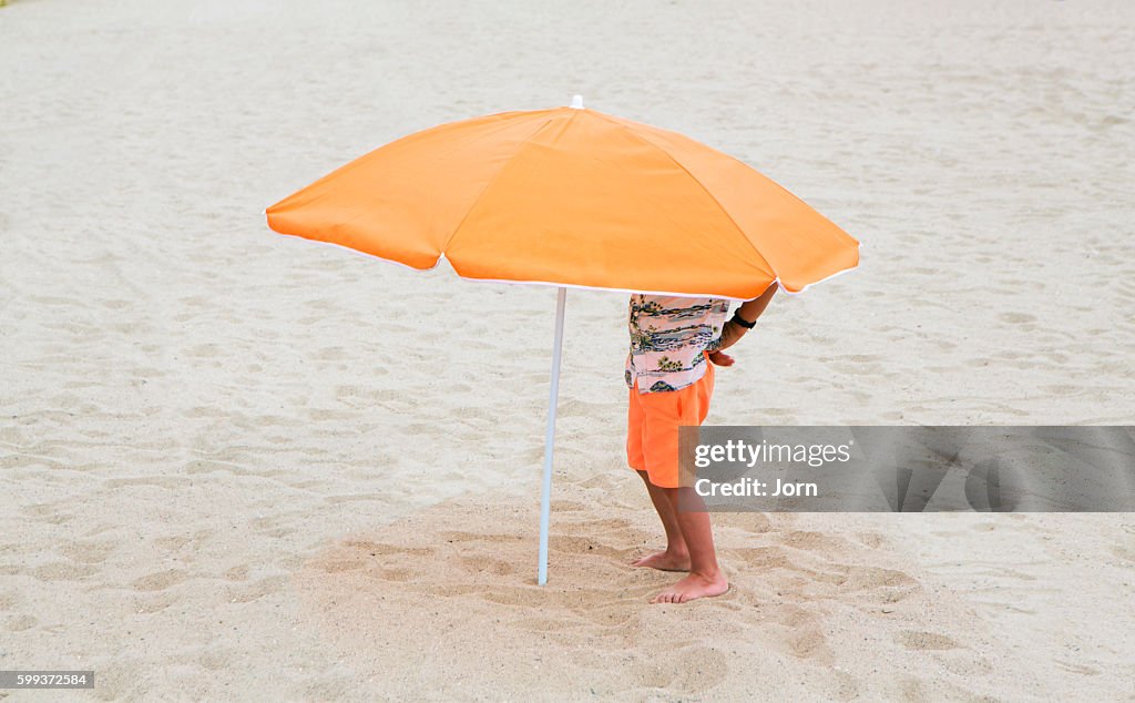 Boy standing under beach umbrella