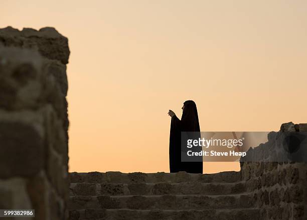 muslim woman taking photo and silhouetted against sunset at bahrain fort near manama at seef, bahrain - bahrain tourism stock pictures, royalty-free photos & images