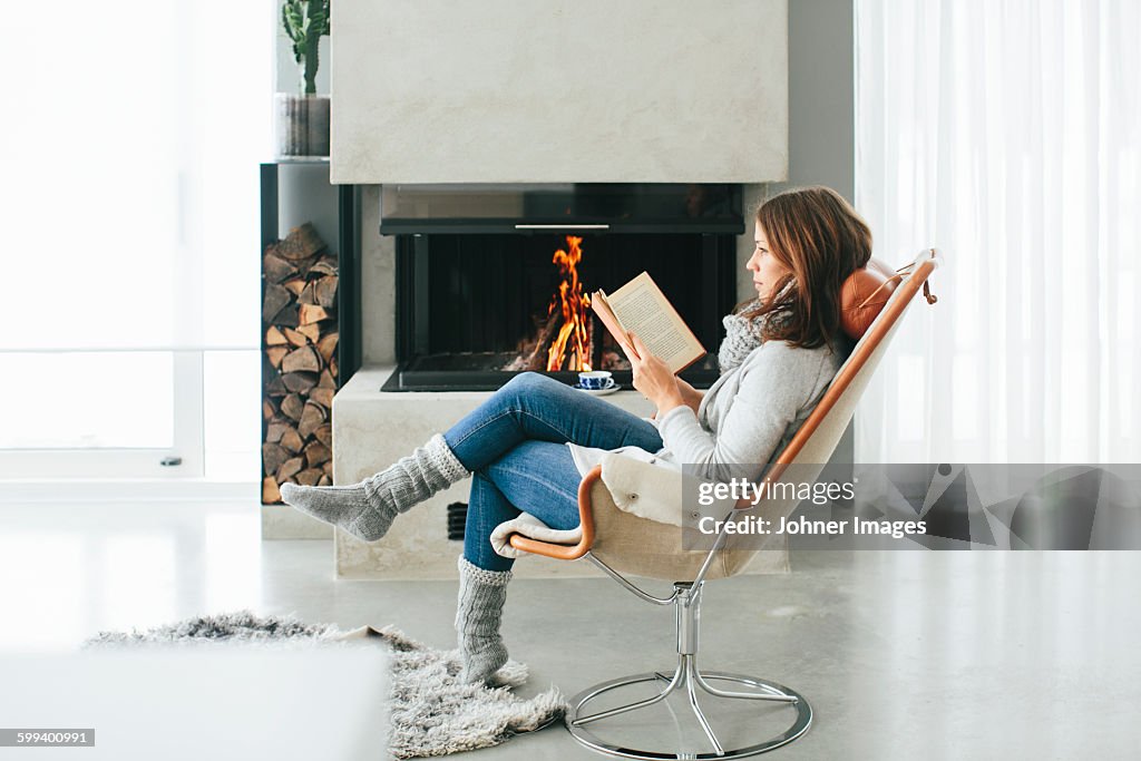 Woman reading book in front of fireplace