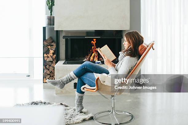 woman reading book in front of fireplace - haardvuur stockfoto's en -beelden