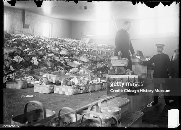 View of Salvation Army food baskets piled up on a stage at Christmas, Chicago, Illinois, 1900s. A Cracker Jack crate is on the stage with the...