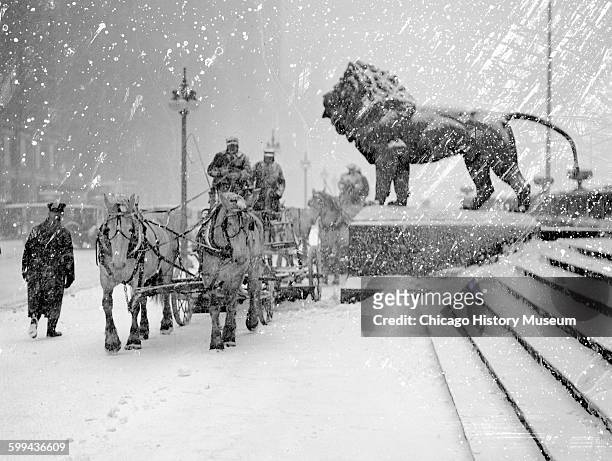 Man driving a horse-drawn wagon on a sidewalk during a snowstorm, next to a bronze lion statue in front of the Art Institute of Chicago, located at...