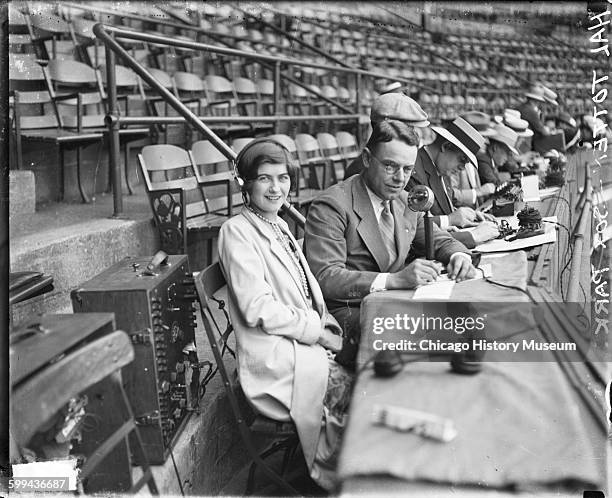 Portrait of Hal Totten, sportswriter and White Sox and Cubs games broadcaster, sitting with an unidentified woman at the announcers' table in...