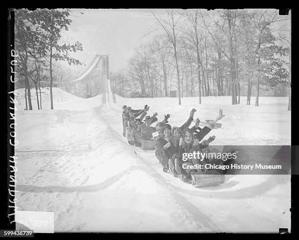 Two groups of women and men sitting and riding on two sleds on snow-covered ground at Medinah Country Club, Medinah, Illinois, 1929.