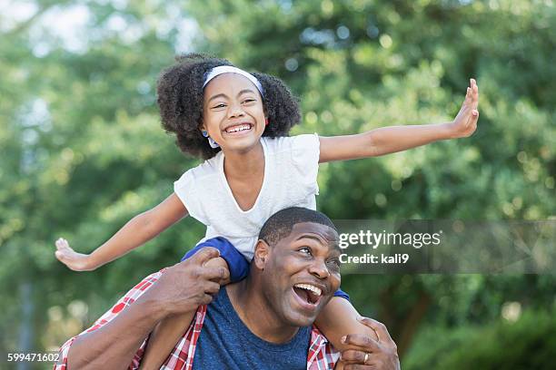 playful mixed race girl sitting on father's shoulders - carrying on shoulders stock pictures, royalty-free photos & images