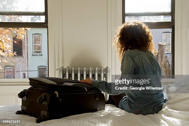 female solo traveller sat on bed in vacation rental company - woman packing suitcase stock pictures, royalty-free photos & images
