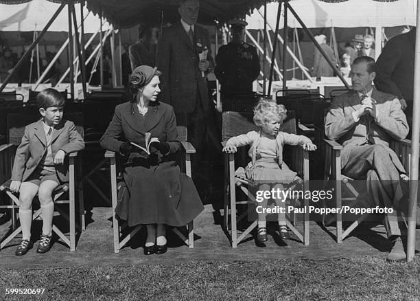 Queen Elizabeth II and Prince Philip, Duke of Edinburgh with their young children, Prince Charles and Princess Anne, all sitting in lawn chairs as...